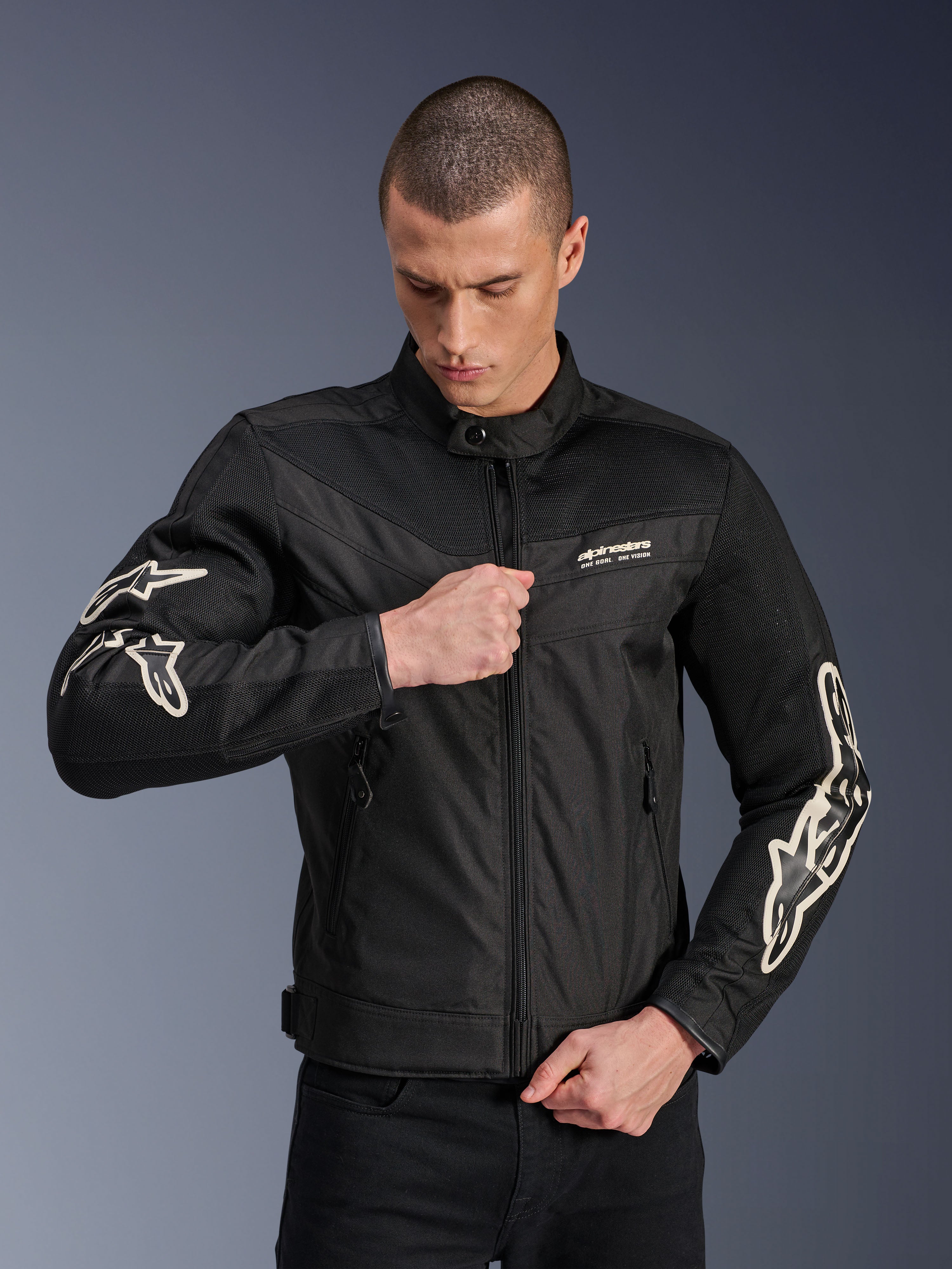 Kurtka Alpinestars T-Dyno Air, czarna, tekstylna kurtka motocyklowa z panelami z siatki 3D i białymi logo na rękawach, noszona przez modela zapinającego zamek, miejski styl jazdy