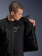 Kurtka Alpinestars T-Dyno Air Jacket, czarna, męski model prezentujący wewnętrzną wyściółkę z siatki oraz metkę wodoodpornej przegrody, produkt założony na czarny t-shirt z grafiką, nowoczesna miejska odzież motocyklowa