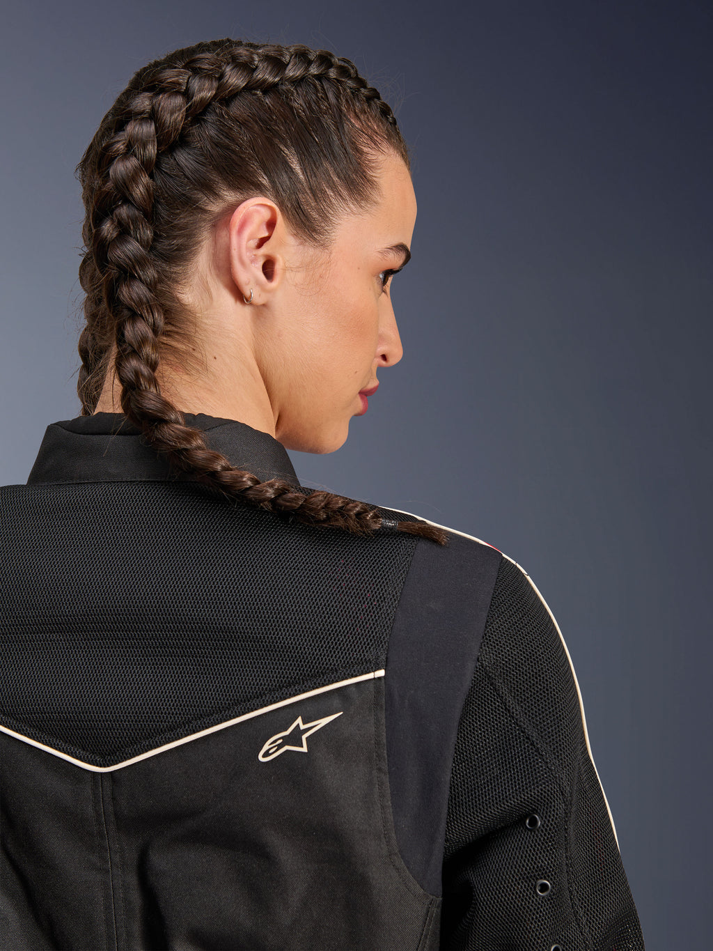 Kobieta w kurtce Alpinestars Stella T-Dyno Air, zbliżenie z tyłu na ramiona i karczek, czarna z oddychającymi panelami z siatki 3D, białe lamówki i małe logo Astars, modelka z zaplecionymi włosami, miejska odzież motocyklowa