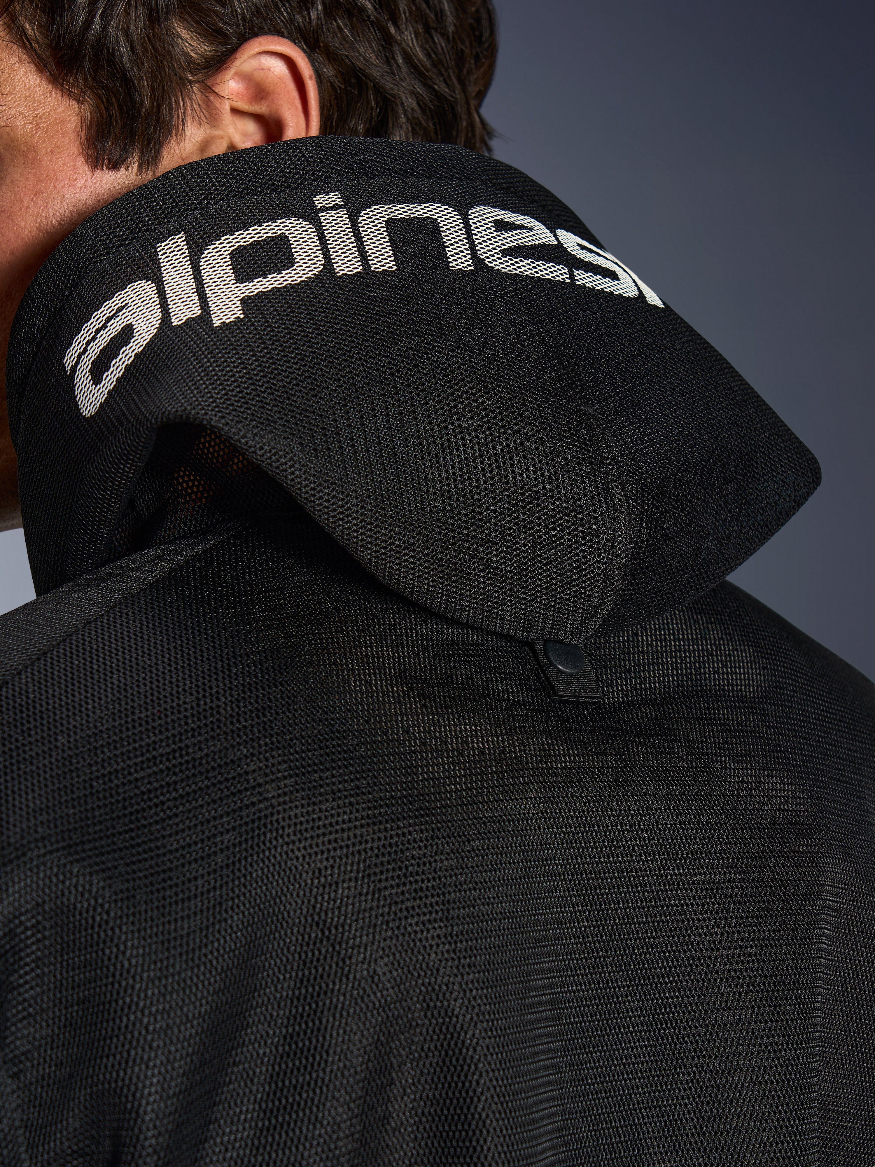 Alpinestars Chrome Superairflow Hoodie, czarna, szczegółowy widok kaptura z siatki 3D z białym brandingiem Alpinestars na górze, widoczny tylny zatrzask stabilizujący, wentylowana tekstylna odzież motocyklowa na ekstremalne upały