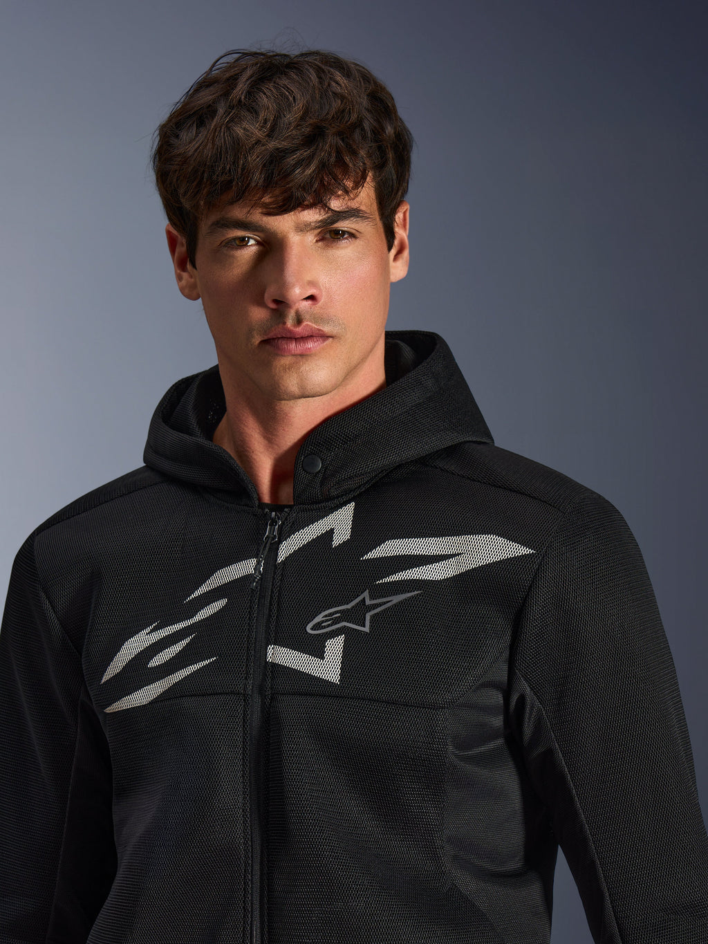 Alpinestars Chrome Superairflow Hoodie, czarna motocyklowa bluza z kapturem, konstrukcja z siatki 3D, duże białe logo graficzne na klatce piersiowej, prezentowana przez modela, miejska odzież sportowa o nowoczesnym, wentylowanym designie
