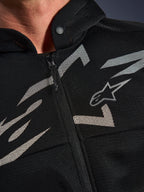 Alpinestars Chrome Superairflow Hoodie, bluza motocyklowa, czarna z biało-szarymi grafikami, zbliżenie na klatkę piersiową pokazujące techniczną konstrukcję z siatki 3D, przedni zamek błyskawiczny i kołnierz zapinany na zatrzask, z logo Alpinestars