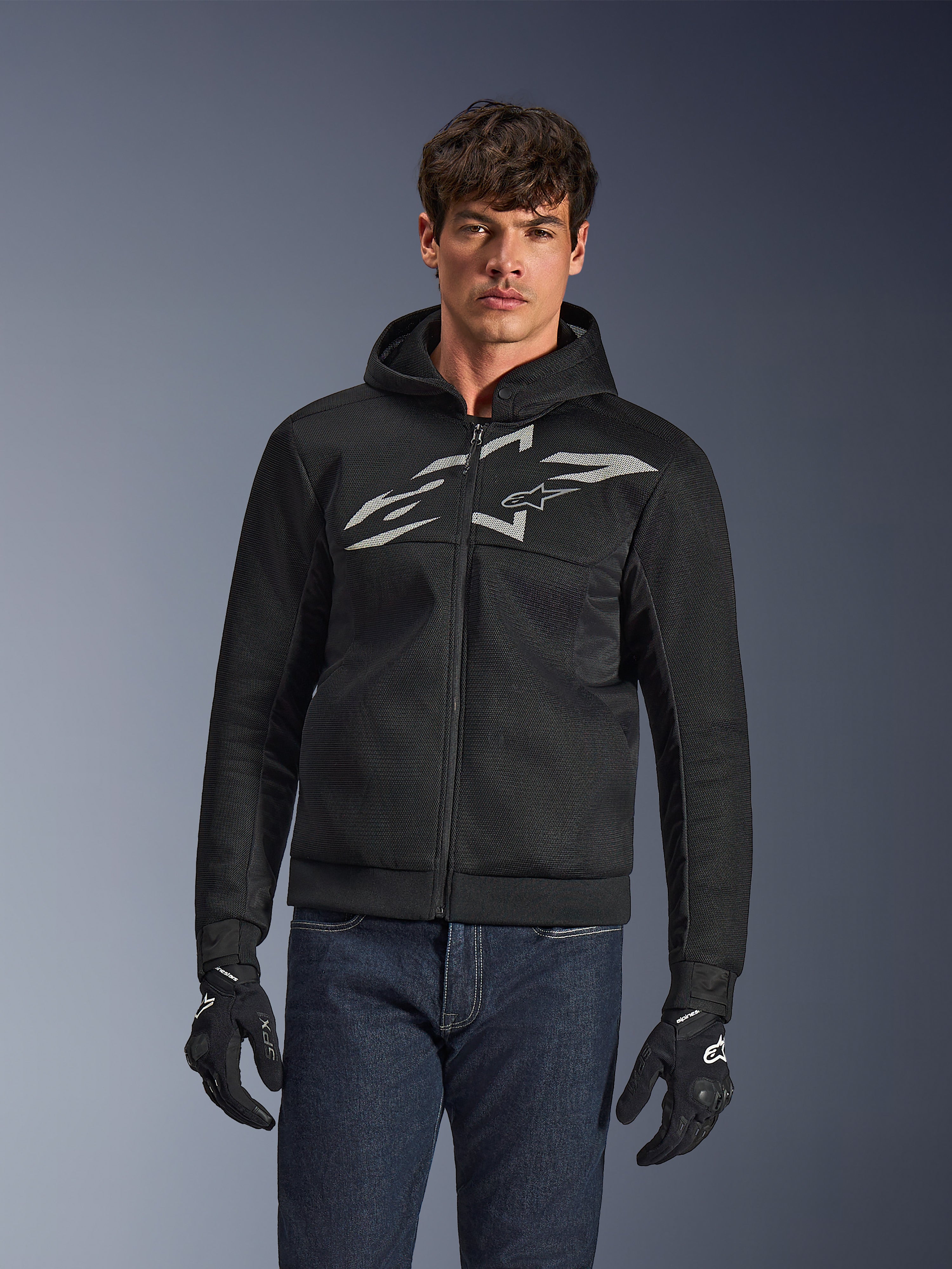 Alpinestars Chrome Superairflow Hoodie, czarna rozpinana bluza motocyklowa z kapturem, duże białe logo na klatce piersiowej, przewiewna konstrukcja z siatki mesh, w zestawieniu z niebieskimi dżinsami i czarnymi rękawicami, sportowa odzież do jazdy miejskiej