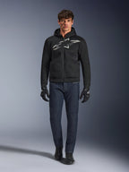 Motocyklista ubrany w bluzę Alpinestars Chrome Superairflow Hoodie w kolorze czarno-szarym, połączoną z ciemnoniebieskimi dżinsami, czarnymi rękawicami motocyklowymi i czarnymi butami. Bluza posiada duże stylizowane logo na piersi oraz strukturę z siatki 3D zapewniającą wydajność w wysokich temperaturach.