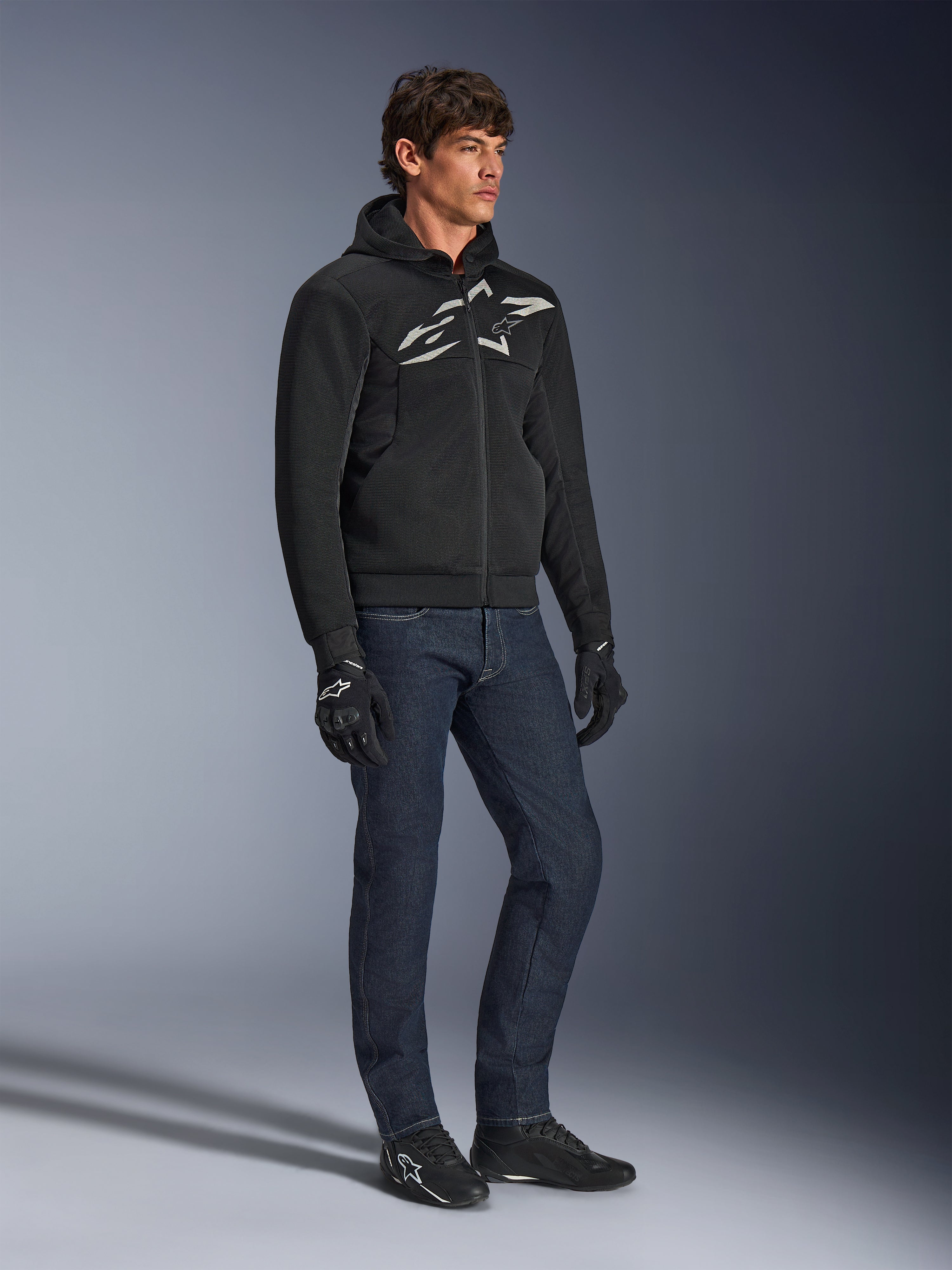Alpinestars Chrome Superairflow Hoodie, czarna z biało-szarym logo, tekstylna konstrukcja z wentylowanej siatki 3D, zestawiona z ciemnoniebieskimi jeansami i czarnymi rękawicami motocyklowymi, miejski sportowy styl jazdy.