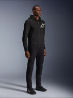 Alpinestars Chrome V2 Sport Hoodie, czarna bluza motocyklowa z białym logo gwiazdy, prezentowana przez modela w pasujących czarnych spodniach i butach motocyklowych typu sneakers, miejska odzież motocyklowa lifestyle