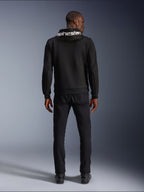 Alpinestars Chrome V2 Sport Hoodie, motocyklowa bluza z kapturem, czarna, widok z tyłu modelu ubranego w czarną bluzę z polaru tech z białym logo Alpinestars na kapturze, w zestawieniu z czarnymi spodniami i butami, casualowy miejski styl jazdy
