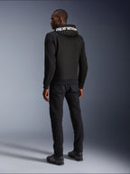 Alpinestars Chrome V2 Sport Hoodie, czarna, widok z tyłu prezentujący biały branding Alpinestars na kapturze, noszona z czarnymi spodniami i butami motocyklowymi, miejska odzież motocyklowa o sportowej sylwetce