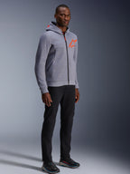 Alpinestars Chrome V2 Sport Hoodie, szary melanż i czerwony fluo, noszona przez modela w czarnych spodniach i ciemnych butach sportowych, z jaskrawopomarańczowym logo gwiazdy na piersi i kapturze, codzienna miejska odzież motocyklowa