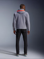 Alpinestars Chrome V2 Sport Hoodie, szary melanż z czerwonymi akcentami fluo, widok z tyłu ukazujący czerwone logo Alpinestars na kapturze, zestawiona z czarnymi spodniami, miejski styl jazdy z ochronną konstrukcją z technicznego polaru