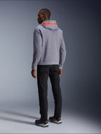 Alpinestars Chrome V2 Sport Hoodie, bluza z kapturem w kolorze szarym melanżowym, widok z tyłu z dużym fluorescencyjnym czerwonym napisem Alpinestars na kapturze, model w czarnych spodniach i ciemnych butach motocyklowych, codzienna miejska odzież motocyklowa