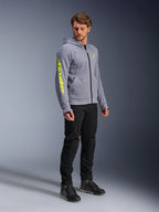 Alpinestars Chrome V2 Sport Hoodie, bluza motocyklowa z kapturem, szary melanż i neonowy żółty, noszona przez modela w czarnych spodniach i butach motocyklowych, wyraziste żółte logo na rękawie i klatce piersiowej, miejska odzież motocyklowa