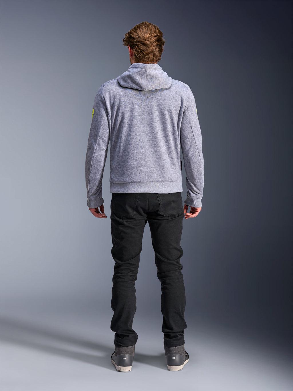Alpinestars Chrome V2 Sport Hoodie, szary melanż z neonowożółtymi akcentami, widok od tyłu miejskiej odzieży motocyklowej, bluza z kapturem z technicznego polaru noszona z czarnymi spodniami, z jaskrawożółtymi detalami na rękawach.