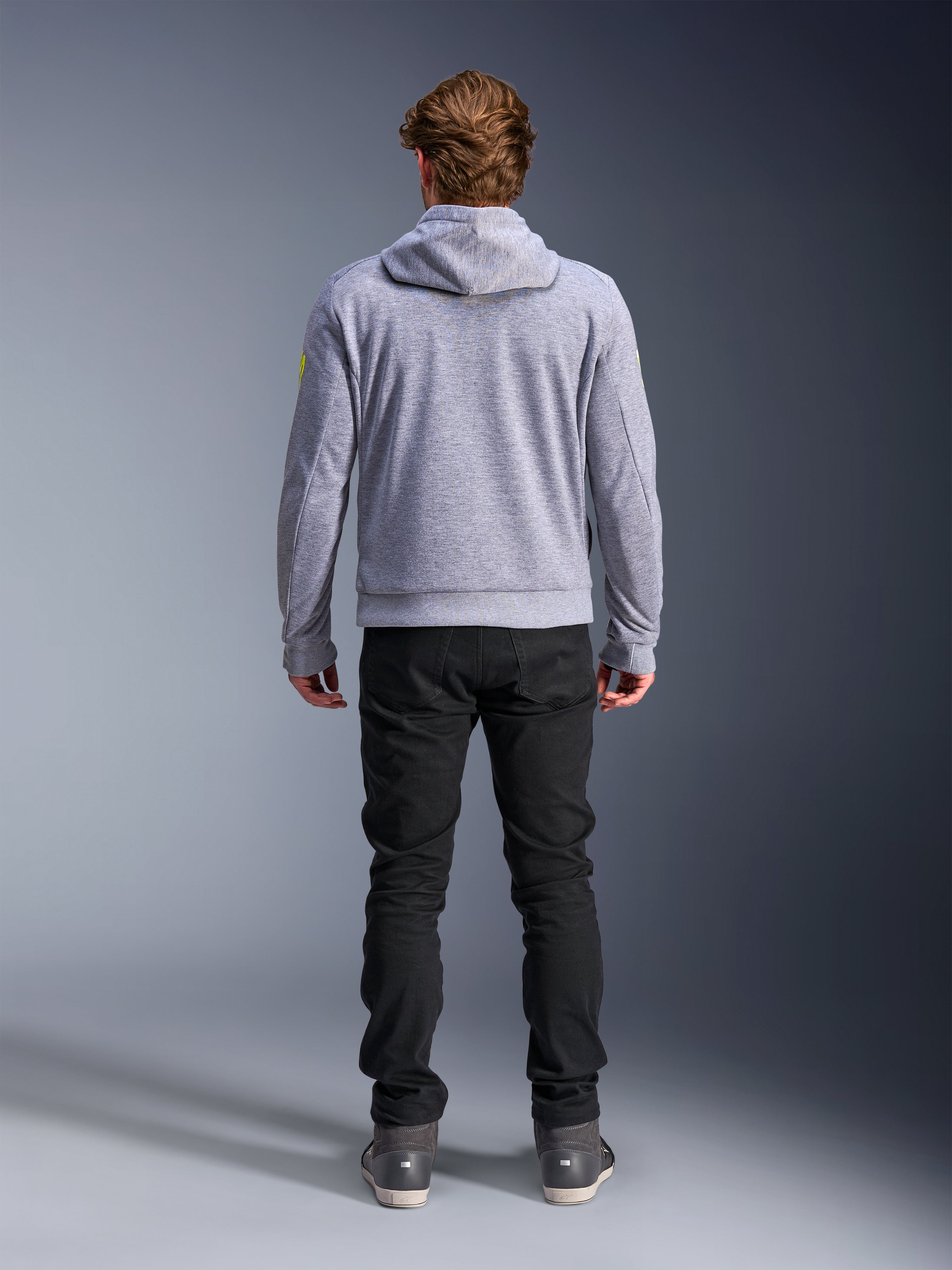 Alpinestars Chrome V2 Sport Hoodie, szary melanż z neonowożółtymi akcentami, widok od tyłu miejskiej odzieży motocyklowej, bluza z kapturem z technicznego polaru noszona z czarnymi spodniami, z jaskrawożółtymi detalami na rękawach.