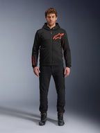 Alpinestars Chrome Air Sport Hoodie, czarno-czerwona fluo, miejska kurtka motocyklowa o konstrukcji z polaru tech, z dużym czerwonym logo Astars na klatce piersiowej i brandingiem na rękawie, noszona przez modela z czarnymi spodniami i butami motocyklowymi