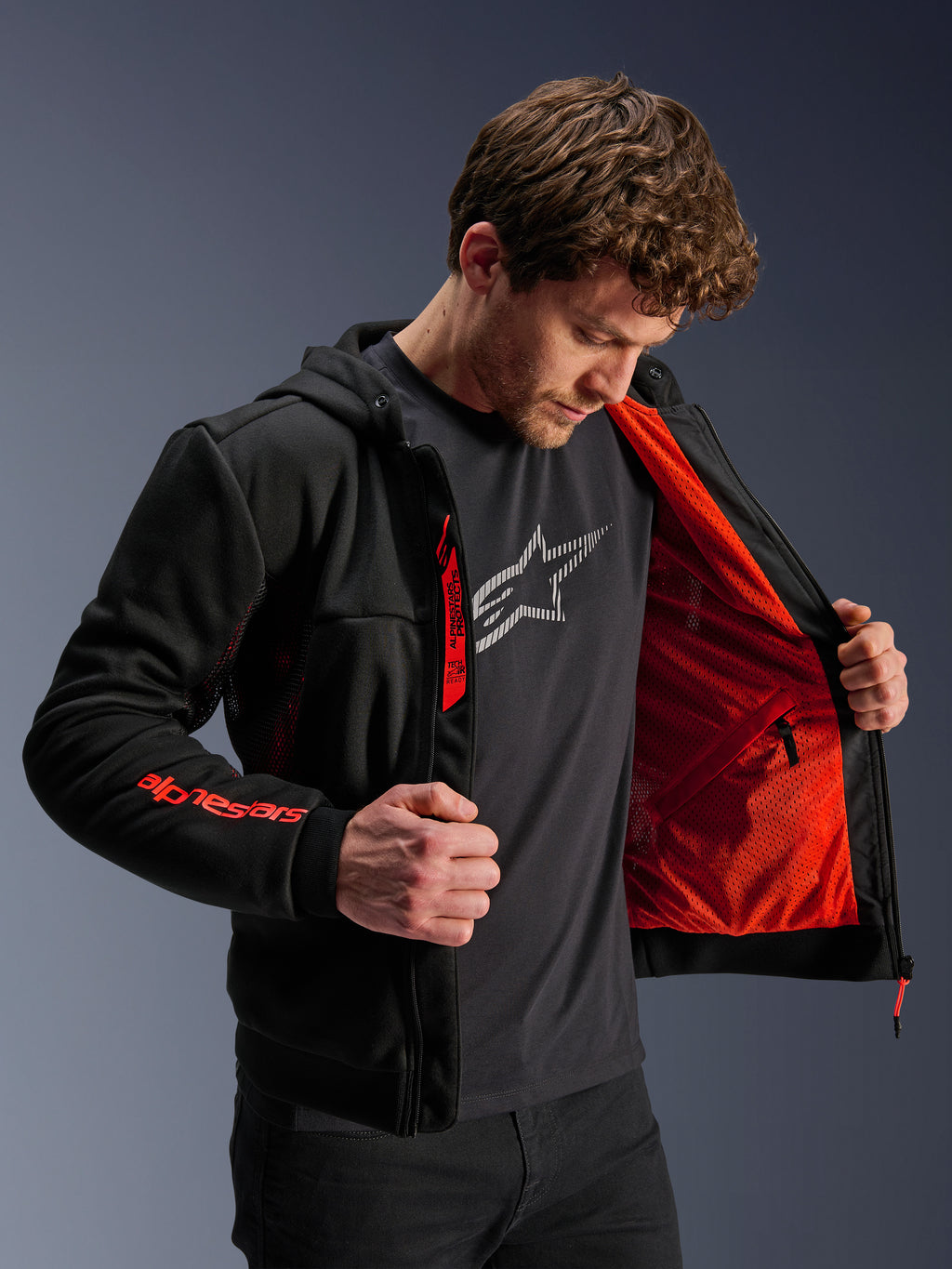 Alpinestars Chrome Air Sport Hoodie w kolorze Black Red Fluo, model otwierający kurtkę, aby zaprezentować jaskrawoczerwoną podszewkę z siatki, branding Alpinestars na prawym rękawie i zamku na piersi, miejska kurtka motocyklowa zaprojektowana dla optymalnego przepływu powietrza.
