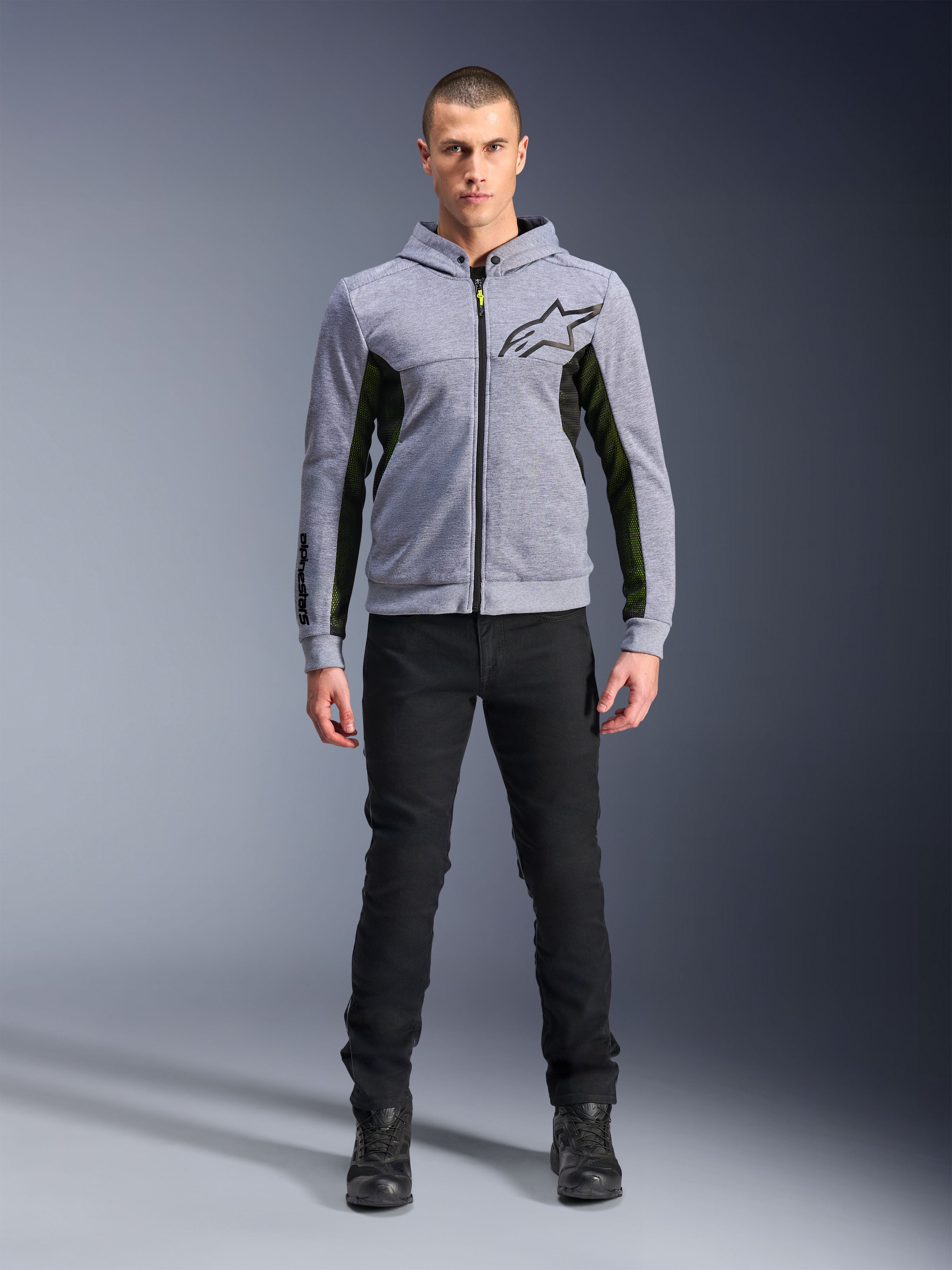 Alpinestars Chrome Air Sport Hoodie, Gray Heather Black, techniczna bluza motocyklowa z czarnymi siatkowymi panelami bocznymi i neonowożółtymi akcentami, czarne logo z gwiazdą na piersi, noszona z czarnymi spodniami i butami, nowoczesny miejski styl jazdy.