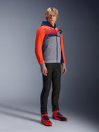 Alpinestars MM93 Chrome V2 Sport Hoodie, miejska bluza motocyklowa, korpus w kolorze szary melanż z granatową klatką piersiową i jaskrawoczerwonymi rękawami fluo, logo 93 na piersi, prezentowana przez modela w czarnych dopasowanych spodniach i pasujących czerwono-niebieskich wysokich butach motocyklowych, nowoczesny sportowy krój do jazdy miejskiej