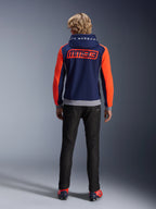 Model od tyłu w bluzie Alpinestars MM93 Chrome V2 Sport Hoodie, granatowa z jaskrawoczerwonymi rękawami Red Fluo i szarymi detalami Gray Mel, duże logo MM93 i Marc Marquez na plecach i kapturze, codzienna bluza motocyklowa w zestawieniu z czarnymi spodniami