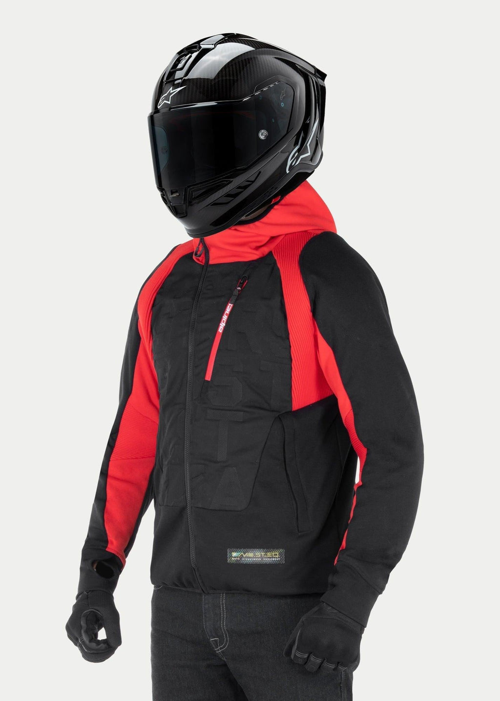 Alpinestars MO.ST.EQ Hybrid Hooded Jacket, miejska bluza motocyklowa, czarno-czerwona, ze skośnym przednim zamkiem i żebrowanymi panelami na ramionach, noszona z czarnym kaskiem integralnym i czarnymi rękawicami, nowoczesny styl streetwearowy