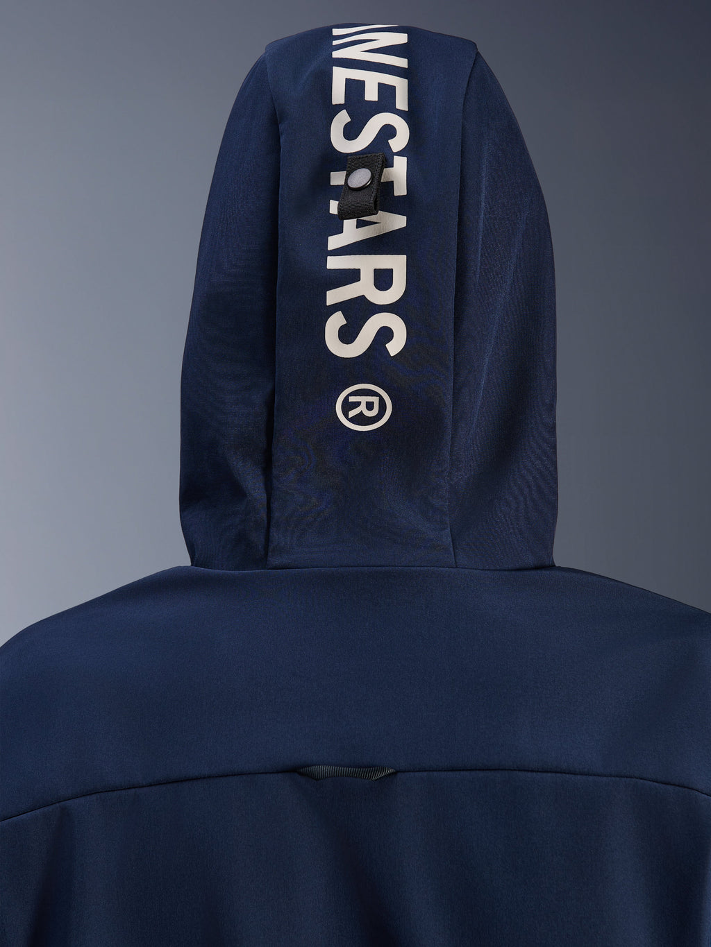 Alpinestars Radium Tech Hoodie w kolorze Night Navy Royal Blue, zbliżenie na tył kaptura z pionowym białym brandingiem Alpinestars i systemem mocowania na pętlę, miejska techniczna odzież motocyklowa