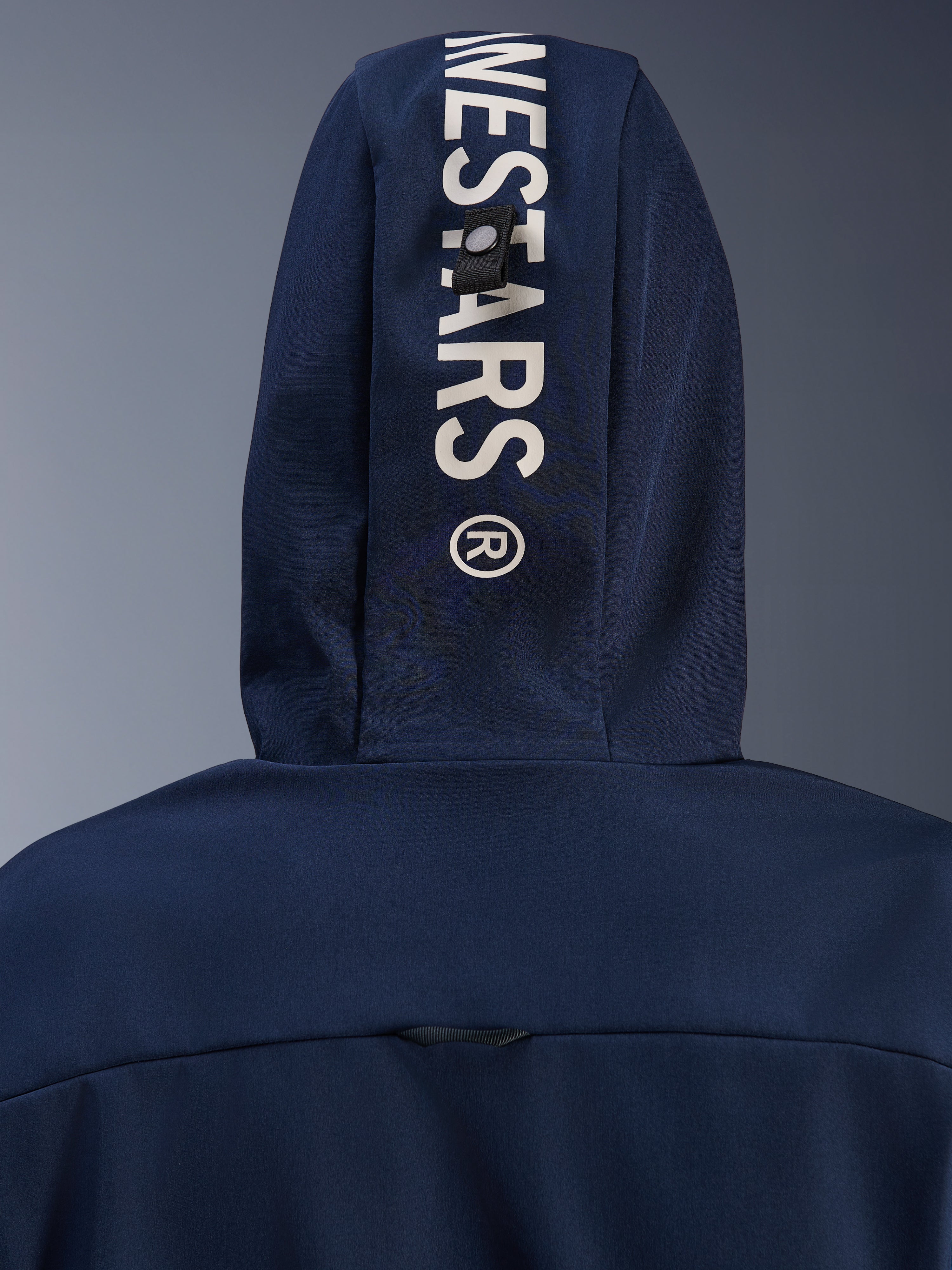 Alpinestars Radium Tech Hoodie w kolorze Night Navy Royal Blue, zbliżenie na tył kaptura z pionowym białym brandingiem Alpinestars i systemem mocowania na pętlę, miejska techniczna odzież motocyklowa