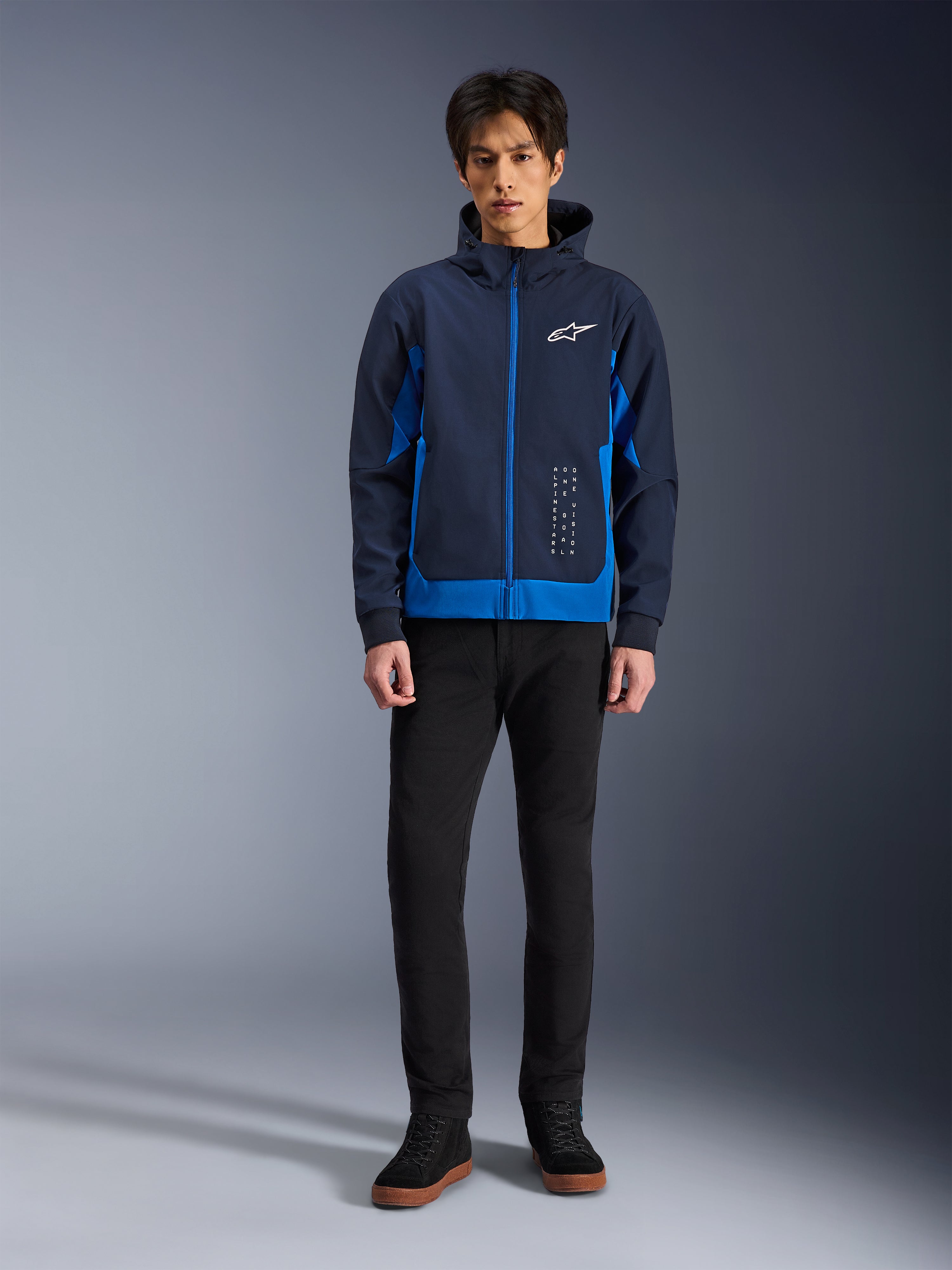 Alpinestars Radium Tech Hoodie, miejska bluza motocyklowa w kolorach Night Navy i Royal Blue, wiatroszczelna powłoka techniczna, casualowy design streetwearowy, zestawiona z czarnymi spodniami i wysokimi sneakersami, białe logo na piersi