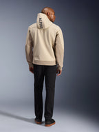 Alpinestars Radium Tech Hoodie, Mastic Aluminum, widok z tyłu pokazujący pionowy napis „ALPINE” na kapturze, techniczna 3-warstwowa wiatroszczelna miejska kurtka motocyklowa z beżowymi panelami, noszona z czarnymi spodniami