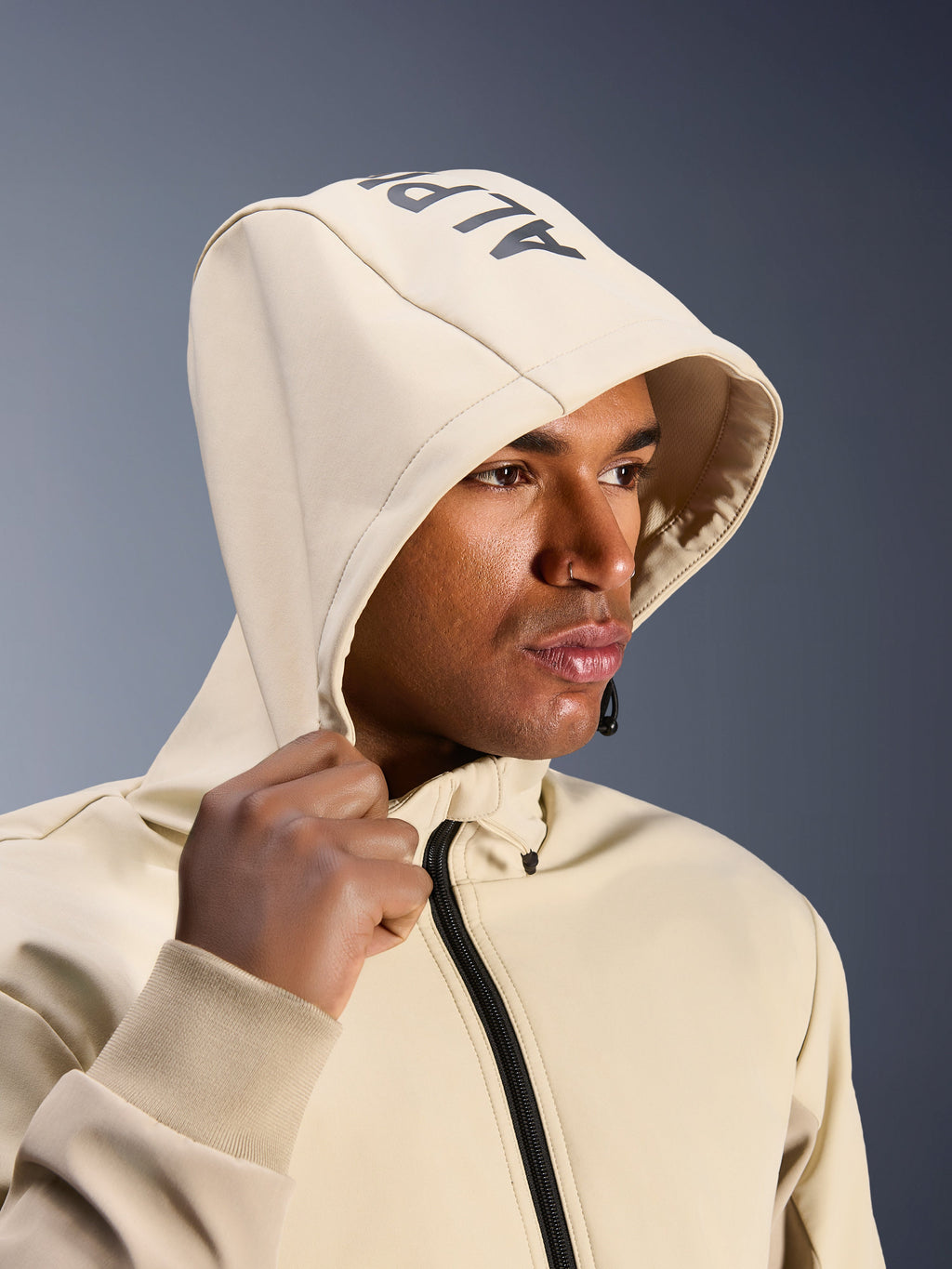 Alpinestars Radium Tech Hoodie w kolorze Mastic Aluminum, zbliżenie na mężczyznę z założonym kapturem i widocznym brandingiem Alpinestars na górze, miejska kurtka motocyklowa z techniczną wiatroszczelną powłoką, nowoczesna estetyka streetwearowa do jazdy po mieście