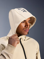 Alpinestars Radium Tech Hoodie w kolorze Mastic Aluminum, zbliżenie na mężczyznę z założonym kapturem i widocznym brandingiem Alpinestars na górze, miejska kurtka motocyklowa z techniczną wiatroszczelną powłoką, nowoczesna estetyka streetwearowa do jazdy po mieście