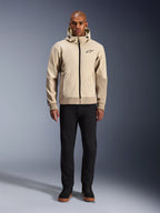 Alpinestars Radium Tech Hoodie w kolorze Mastic Aluminum, miejska bluza motocyklowa prezentowana na modelu w czarnych spodniach i butach, z czarnym zamkiem błyskawicznym na całej długości, małym logo na piersi, o sportowym kroju do jazdy miejskiej