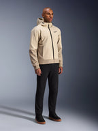 Alpinestars Radium Tech Hoodie, miejska kurtka motocyklowa, jasnobeżowy Mastic Aluminum, noszona z czarnymi spodniami i czarnymi wysokimi sneakersami, wyposażona w techniczną wiatroszczelną powłokę, przedni zamek błyskawiczny i odpinany kaptur, nowoczesny design streetwearowy do jazdy miejskiej