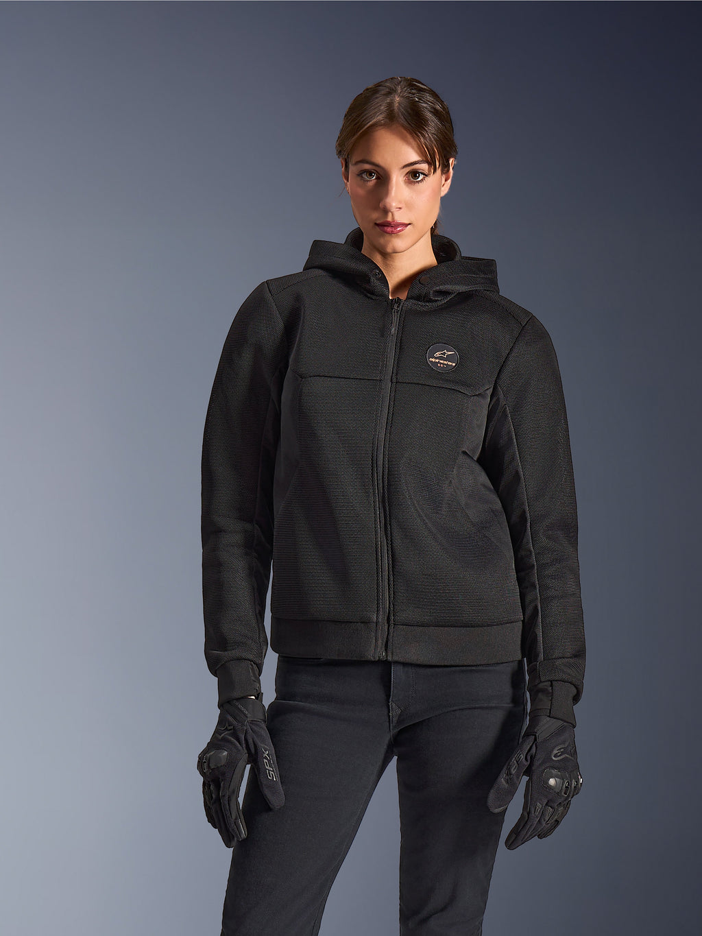 Alpinestars Stella Chrome Superairflow Hoodie, damska bluza motocyklowa z kapturem, czarna, z logo na klatce piersiowej i centralnym zamkiem, noszona z czarnymi rękawicami, nowoczesny design do jazdy miejskiej