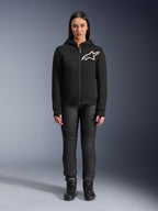 Kobieta w bluzie z kapturem Alpinestars Stella Chrome V2 Sport Hoodie, czarna z białym logo Astars na klatce piersiowej, zestawiona z czarnymi technicznymi spodniami motocyklowymi i butami, miejski styl odzieży motocyklowej.