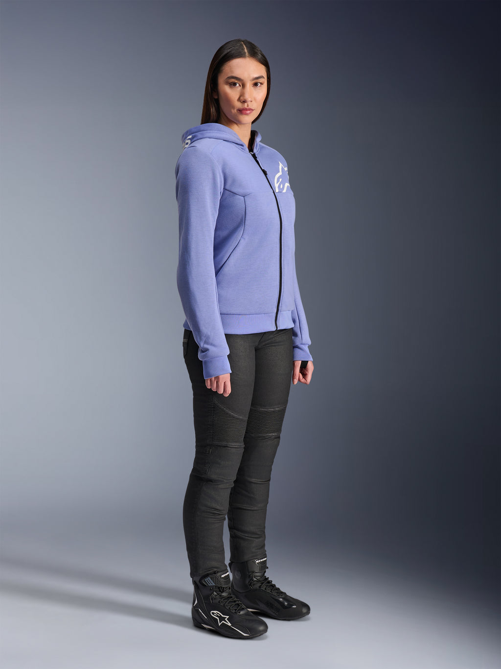 Alpinestars Stella Chrome V2 Sport Hoodie, damska bluza motocyklowa w kolorze niebiesko-fioletowym z białym logo Alpinestars na piersi, prezentowana na modelce z czarnymi spodniami i butami motocyklowymi, miejska odzież motocyklowa dla kobiet