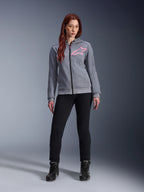 Alpinestars Stella Chrome V2 Sport Hoodie, kolor szary melanż z neonowym różem, noszona przez kobietę w czarnych spodniach i butach, różowe logo gwiazdy Alpinestars na piersi, miejska odzież motocyklowa z pełnym zamkiem, lekki polar techniczny o sportowym kroju.