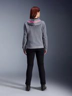 Alpinestars Stella Chrome V2 Sport Hoodie, damska bluza motocyklowa, kolor szary melanż i różowy fluo, widok z tyłu prezentujący różowe logo Alpinestars na kapturze, noszona z czarnymi spodniami i butami motocyklowymi, codzienna odzież motocyklowa dla kobiet
