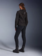 Alpinestars Stella Radium Tech Hoodie, czarna damska bluza motocyklowa do jazdy miejskiej, widok z tyłu prezentujący napis „ALPIN” na kapturze, zestawiona z czarnymi technicznymi spodniami motocyklowymi i czarnymi butami, lekka wiatroszczelna powłoka techniczna.