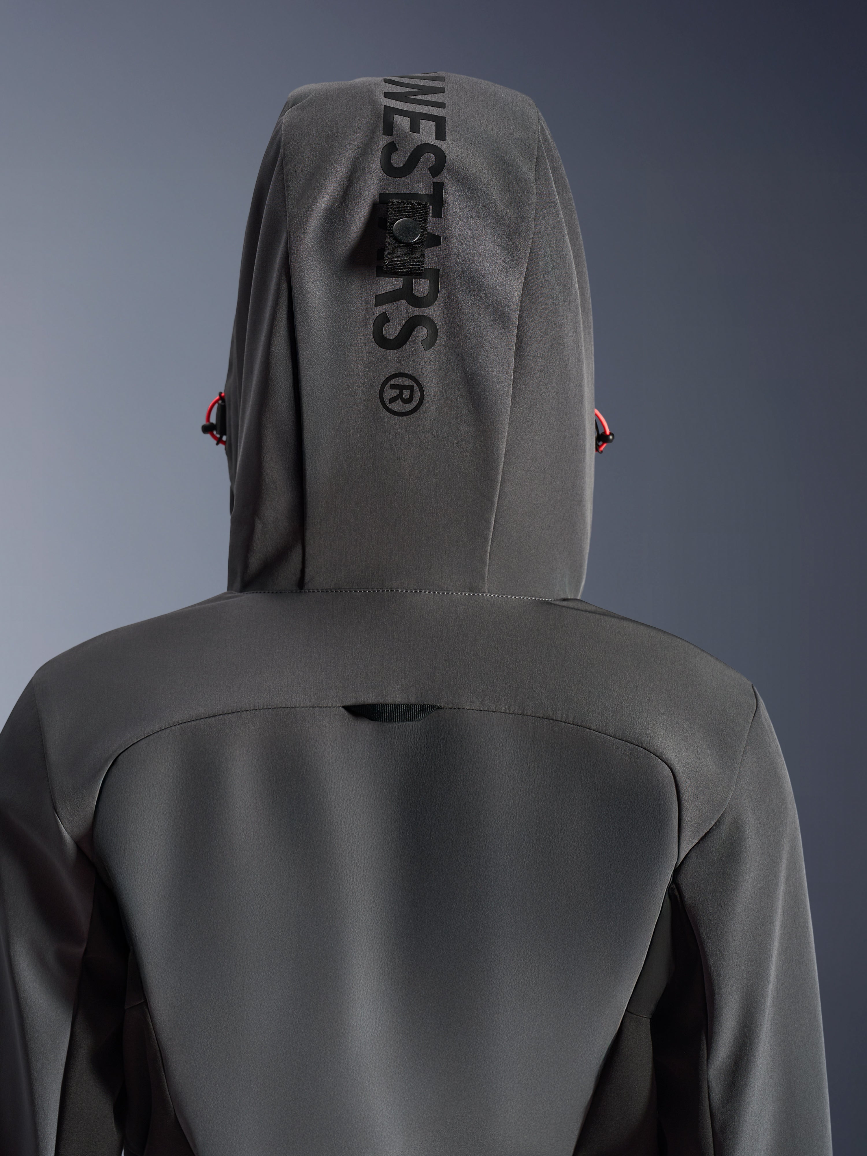 Alpinestars Woman Stella Radium Tech Hoodie, kolor Deep Gray Black, zbliżenie na tył pokazujące kaptur z pionowym brandingiem i pętlą mocującą, czerwone akcenty ściągaczy, wytrzymała 3-warstwowa wiatroszczelna konstrukcja tekstylna do jazdy miejskiej.