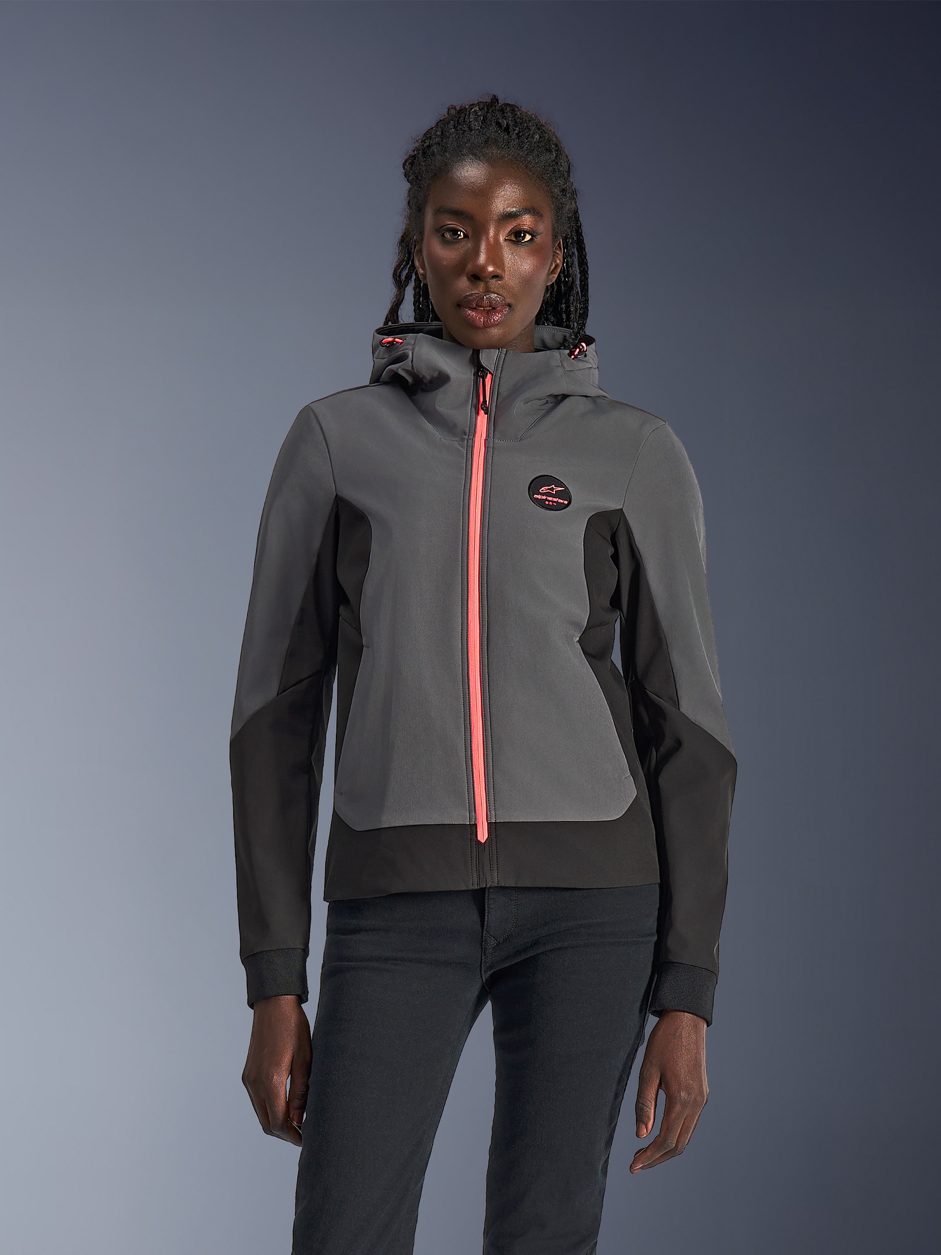 Alpinestars Stella Radium Tech Hoodie, damska bluza motocyklowa z kapturem, ciemnoszara i czarna z jaskraworóżowym zamkiem i sznurkami przy kapturze, prezentowana na modelce, sportowy miejski design z logo Alpinestars na piersi