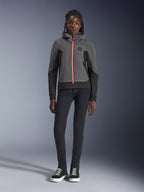 Modelka w bluzie Alpinestars Stella Radium Tech Hoodie, kolor ciemnoszary i czarny z jaskrawopomarańczowym akcentem zamka, miejska bluza motocyklowa, w zestawieniu z czarnymi spodniami typu slim i sneakersami, casualowa odzież sportowa dla kobiet