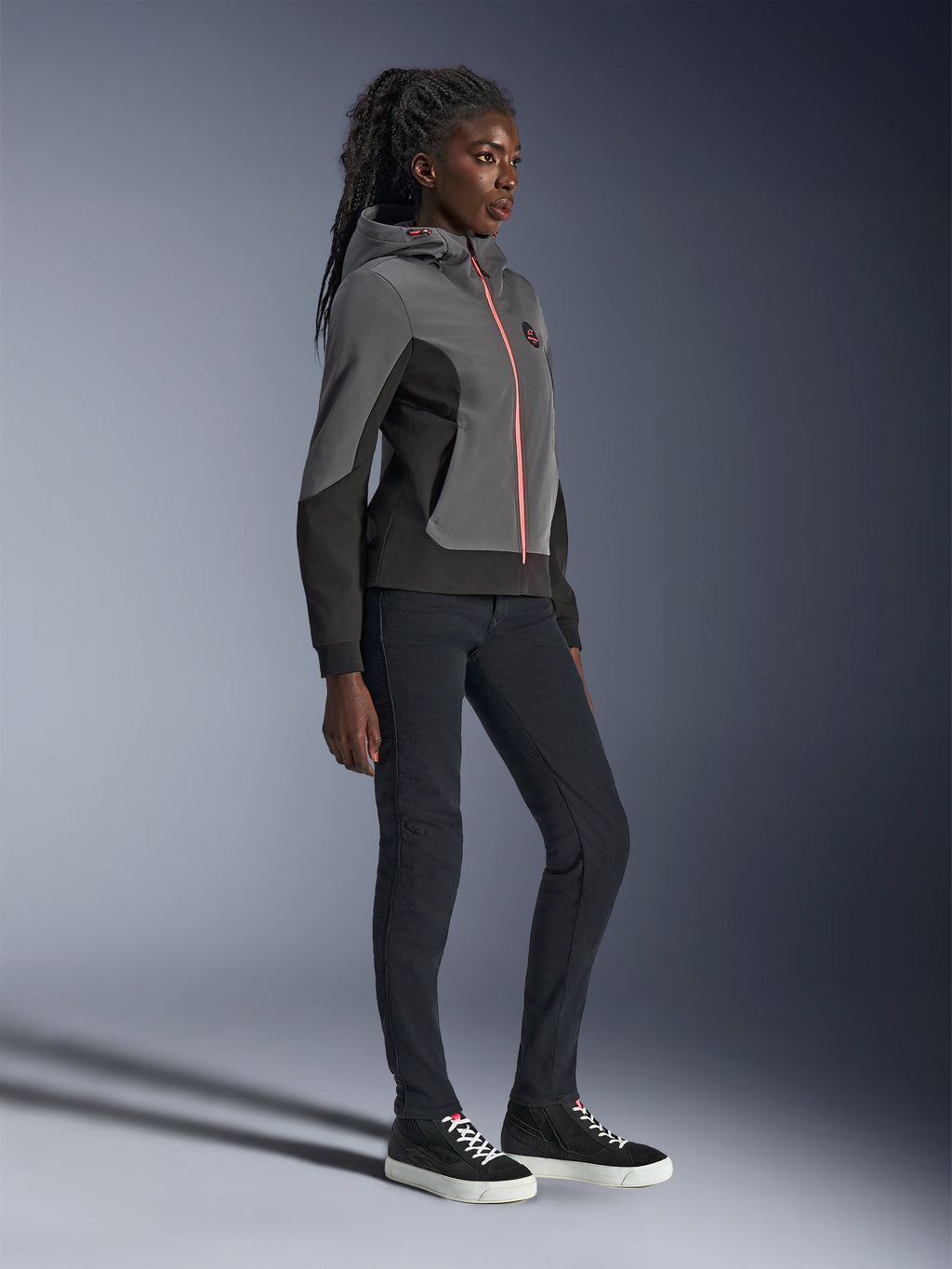 Alpinestars Stella Radium Tech Hoodie, miejska bluza motocyklowa, ciemnoszara i czarna z jasnopomarańczowym zamkiem, zestawiona z czarnymi spodniami i czarnymi sneakersami, sportowy krój dopasowany do kobiecej sylwetki
