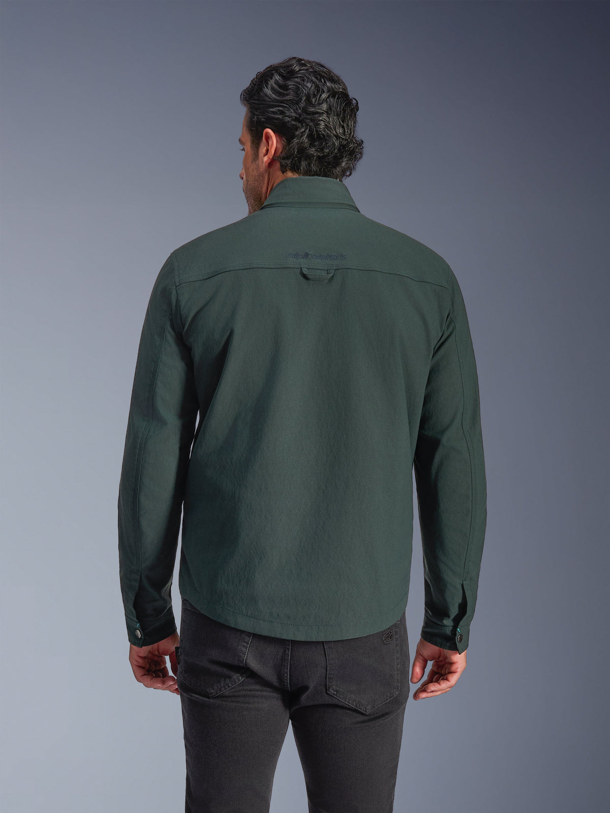 Alpinestars Bryon Water Resistant Overshirt, ciemnozielona (Dark Emerald), widok z tyłu na modelu, haftowane logo w górnej części pleców, trwałe woskowane płótno, miejska kurtka motocyklowa w zestawieniu z ciemnymi spodniami