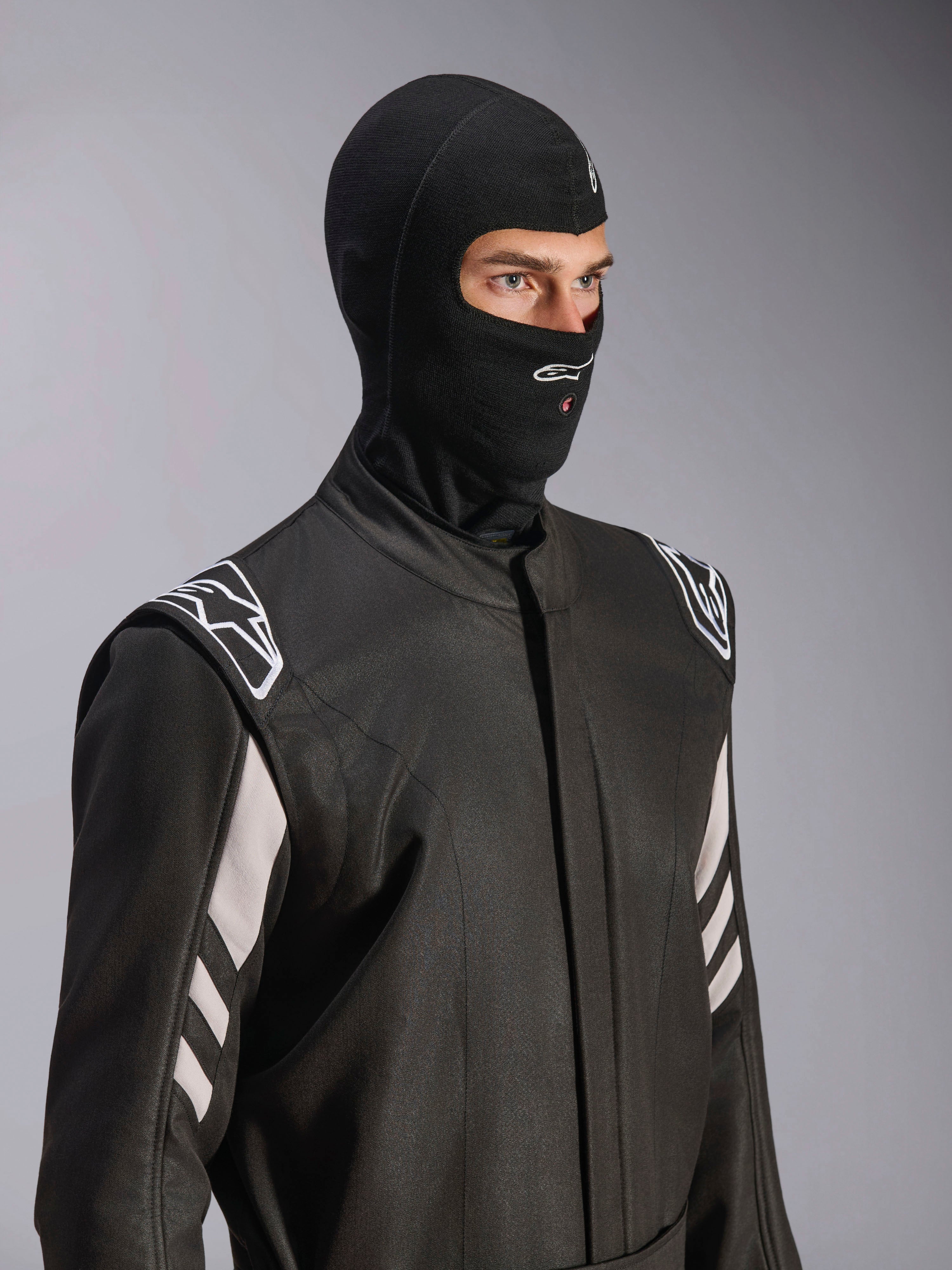 Kominiarka Alpinestars ZX Evo V3, czarna, ognioodporna kominiarka wyścigowa, noszona przez modela w czarnym kombinezonie z białymi akcentami, logo Alpinestars na podbródku, otwór na rurkę nawadniającą, profesjonalny sprzęt ochronny do sportów motorowych