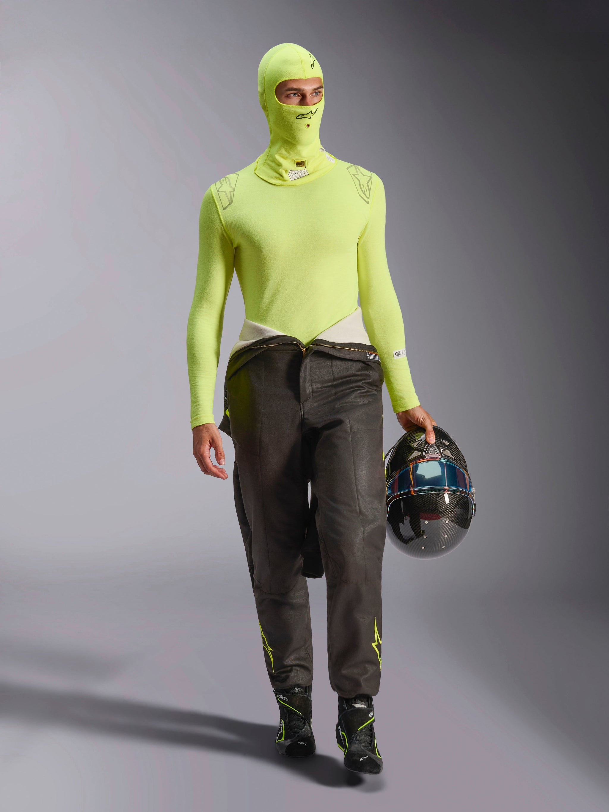 Kierowca wyścigowy ubrany w kominiarkę Alpinestars ZX Evo V3 w kolorze Yellow Fluo, dopasowana koszulka termoaktywna z długim rękawem, ciemne spodnie wyścigowe, czarne buty wyścigowe, kask z włókna węglowego, profesjonalny sprzęt do wyścigów samochodowych