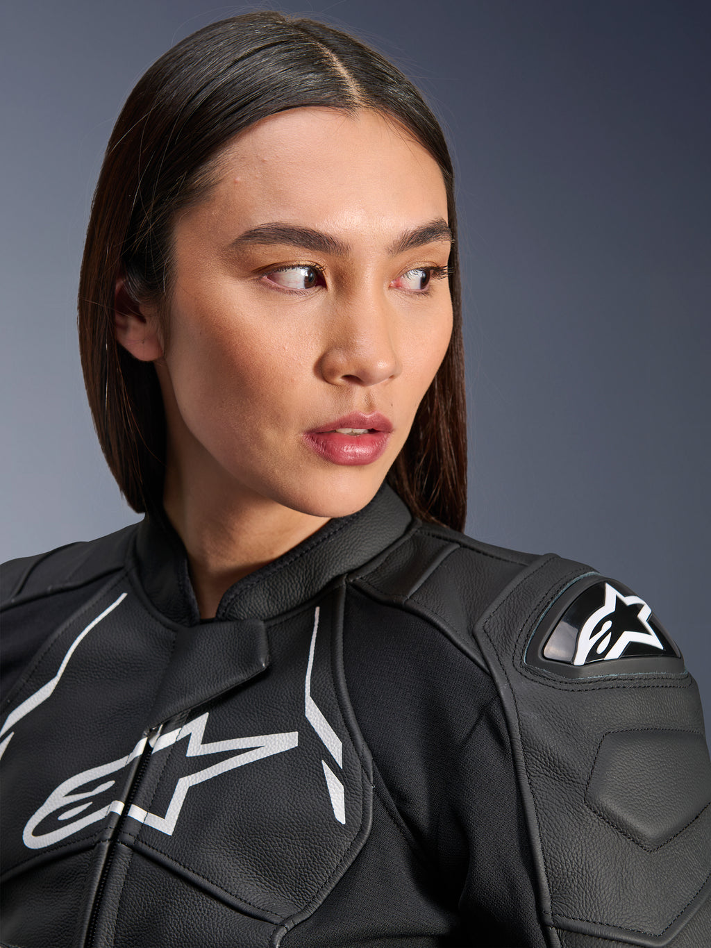 Kobieta w skórzanej kurtce Alpinestars Stella Dusk w kolorze czarno-białym, zbliżenie na białe logo Alpinestars na klatce piersiowej i zewnętrzny ochraniacz ramion DFS, najwyższej jakości skórzana konstrukcja do motocyklowych wyścigów drogowych