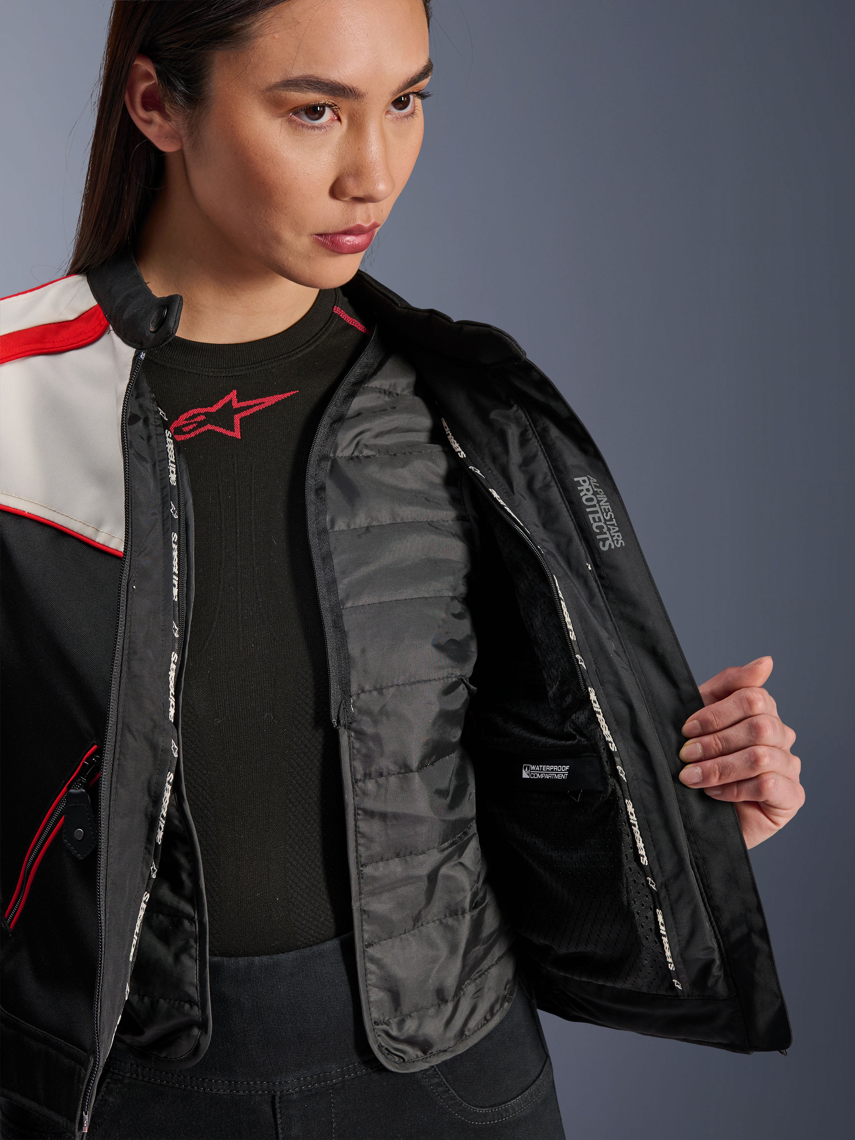Alpinestars Stella T-Dyno WR Jacket, damska kurtka motocyklowa, czarna, ekri i jaskrawoczerwona, zbliżenie na wnętrze pokazujące odpinaną pikowaną kamizelkę termiczną, wodoodporną przegrodę wewnętrzną oraz branding „ALPINESTARS PROTECTS”