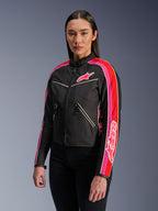 Kobieta w kurtce Alpinestars Stella T-Dyno WR w kolorze Black Bright Red Fuchsia, tekstylna kurtka motocyklowa o kroju inspirowanym stylem vintage, z wyrazistymi fuksjowymi i czerwonymi pasami na rękawach oraz logo na piersi, zestawiona z czarnymi spodniami.