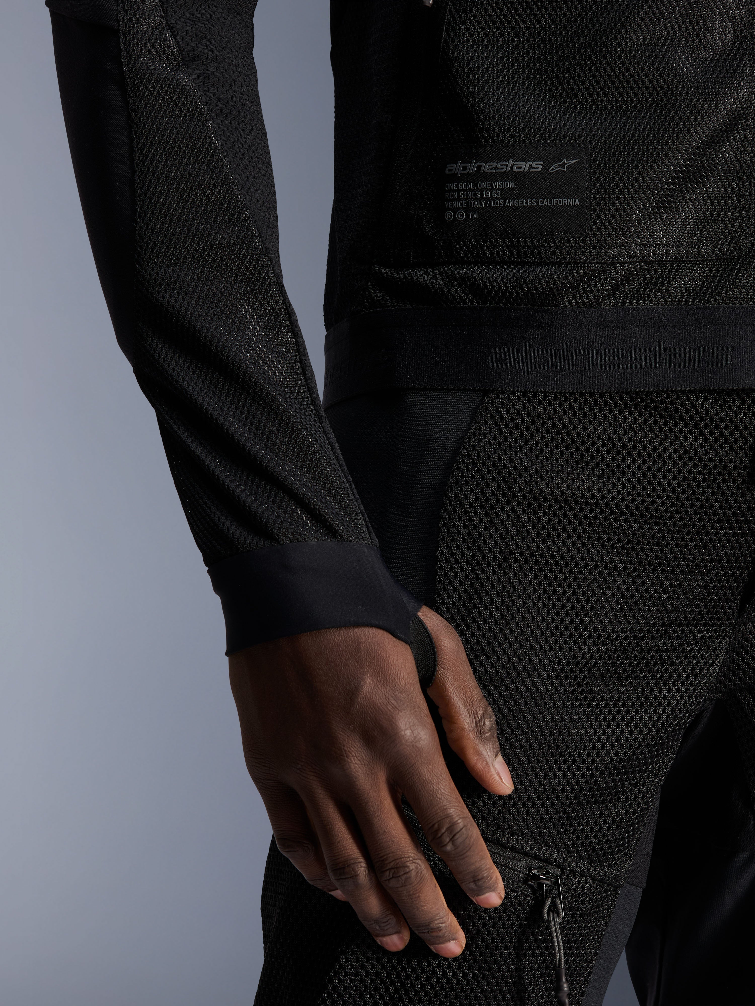 Alpinestars Troop-Air Jacket, czarna, zbliżenie na techniczną konstrukcję z siatki, markowa naszywka z tekstem technicznym, rękaw ze zintegrowanym otworem na kciuk, miejska letnia kurtka motocyklowa zapewniająca wysoki przepływ powietrza