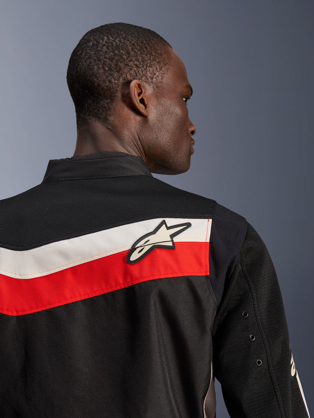 Kurtka Alpinestars T-Dyno Air, Black Bright Red Ecru, zbliżenie na górną część pleców i ramię, poziome czerwone i ecru pasy z białym logo Astars, oddychające panele z siatki 3D na karczku i rękawach, nowoczesna klasyczna tekstylna kurtka motocyklowa